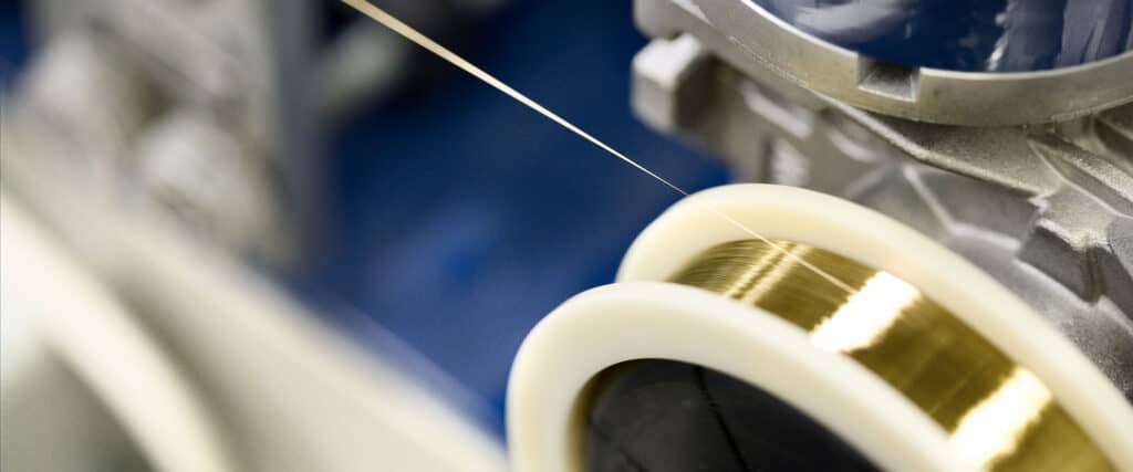 Close-up of precision gold plating on ultra-fine wire during manufacturing for medical, aerospace, and electronics use.